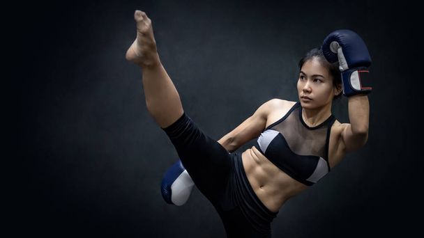 Young Asian woman boxer with blue boxing gloves kicking in the exercise gym, Martial arts on black background. Female boxing class concept - Photo, Image