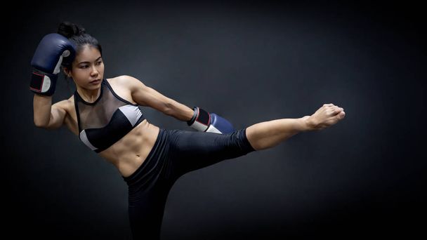 Joven mujer asiática boxeadora con guantes de boxeo azul pateando en el gimnasio de ejercicio, artes marciales sobre fondo negro. Concepto de clase de boxeo femenino
 - Foto, imagen
