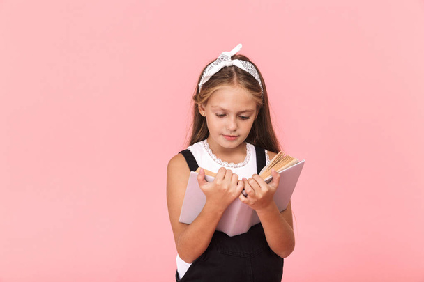 Lovely little girl wearing dress reading a book isolated over pink background - Foto, imagen