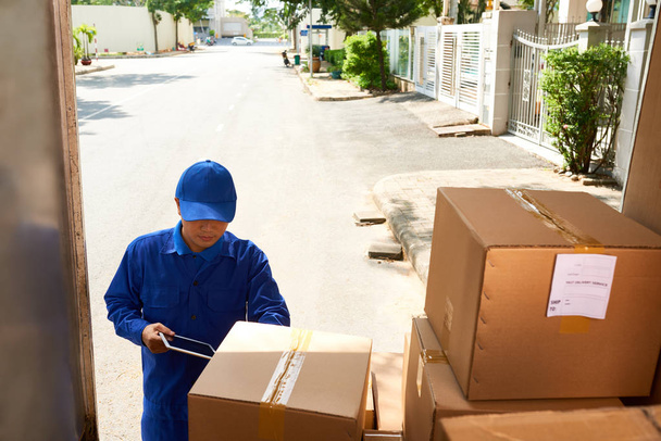 Entrega homem de uniforme azul levando caixas para fora do caminhão
 - Foto, Imagem