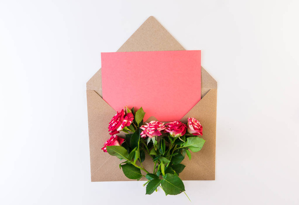 Λουλούδι της σειράς. Κόκκινο λευκό τριαντάφυλλο λουλούδι με πράσινα φύλλα σχετικά με craft φάκελο με κενό κομμάτι ροζ χαρτί σε άσπρο φόντο. Χώρο αντίγραφο για το κείμενο. - Φωτογραφία, εικόνα