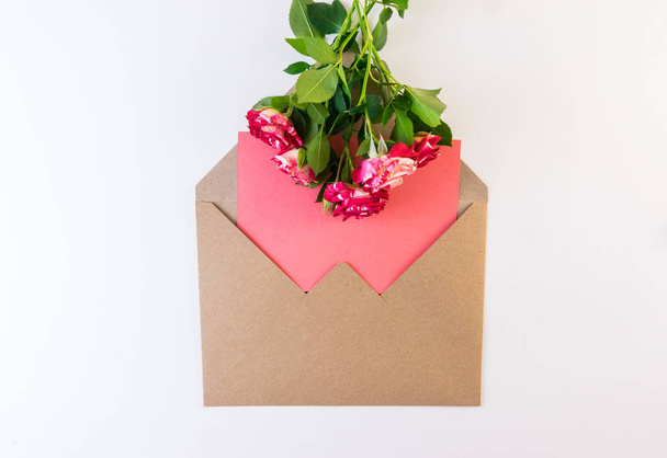 Flower series. Red white rose flower with green leaves on craft envelope with empty piece of pink paper on white background. Copy space for text. - Photo, Image