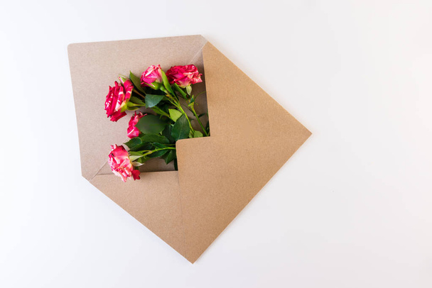 Λουλούδι της σειράς. Κόκκινο λευκό τριαντάφυλλο λουλούδι με πράσινα φύλλα σχετικά με craft φάκελο σε λευκό φόντο. - Φωτογραφία, εικόνα