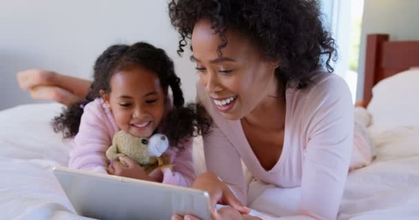 Front view of black mother and daughter using digital tablet at comfortable home. Black mother and daughter relaxing in bedroom 4k - Felvétel, videó