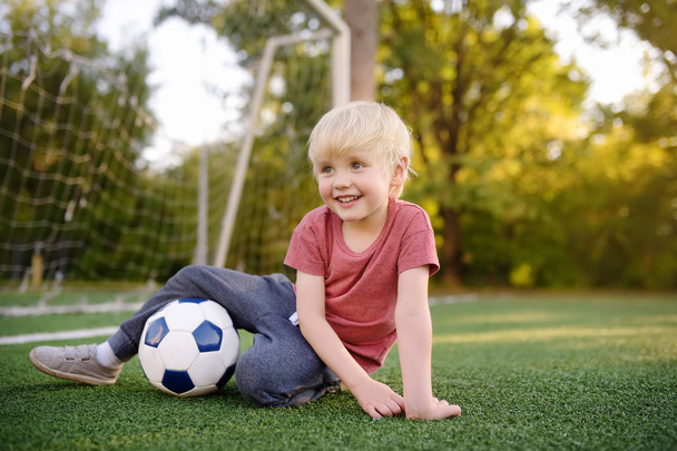 Little boy having fun playing a soccer/football game on summer day. Active outdoors game/sport for children. Kids soccer classes and camps - Photo, image