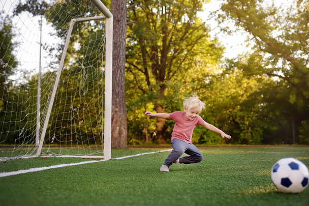 Little boy having fun playing a soccer/football game on summer day. Active outdoors game/sport for children. Kids soccer classes and camps - Foto, afbeelding