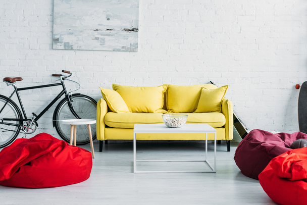 geräumiges möbliertes Wohnzimmer mit gemütlichen Sitzsäcken und bequemem gelben Sofa - Foto, Bild