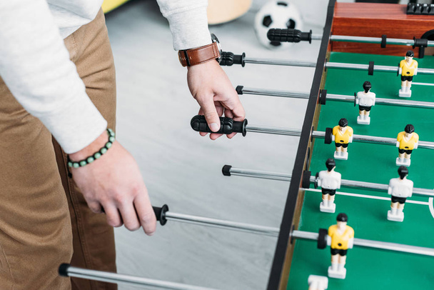 cropped view of man in white sweatshirt and brown jeans playing table football - Fotografie, Obrázek