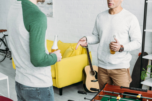 частковий вид чоловіків, що стоять у вітальні і тримають пляшки пива
  - Фото, зображення