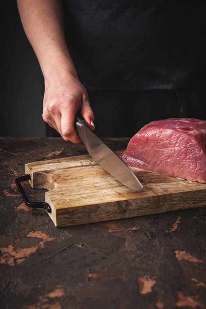 female hands cut raw pork on a wooden board in the kitchen - Foto, immagini
