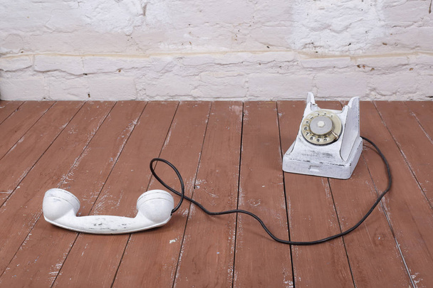 weißes Vintage-Telefon mit dem Tonabnehmer auf braunem Holz und weißem Wandhintergrund - Foto, Bild