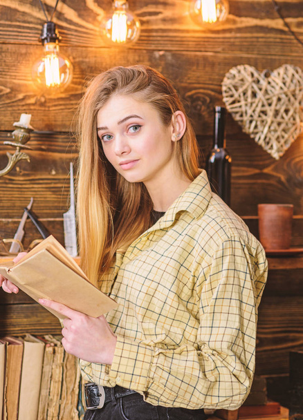 Girl reading poetry in warm atmosphere. Lady on dreamy face in plaid clothes holds book, reading poetry. Girl in casual outfit in wooden vintage interior enjoy poetry. Poetry evening concept - Valokuva, kuva