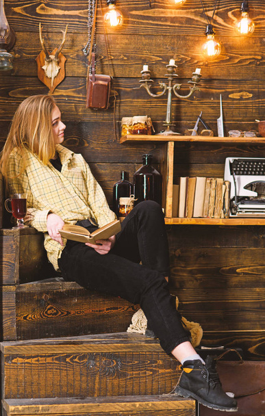 Relaxation concept. Girl student relaxing with book and glass of mulled wine. Girl in casual outfit sits with book in wooden vintage interior. Lady on calm face in plaid clothes looks casual - Foto, Imagem
