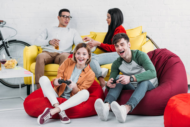 amigos multiculturais felizes jogando videogame e desfrutando de bebidas e lanches em casa festa
 - Foto, Imagem