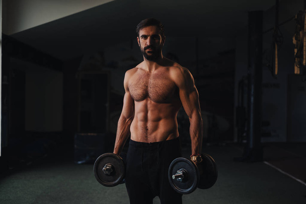 Спортсмен без сорочки з бородою тримає гантелі в спортзалі
 - Фото, зображення