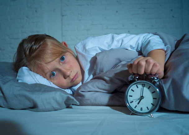 Sweet sleepless little girl lying sad in bed looking at alarm clock having to wake up but feeling tired sleepless in Troubles staying asleep Night Terrors Sleep disorder and Children Insomnia concept. - Photo, Image