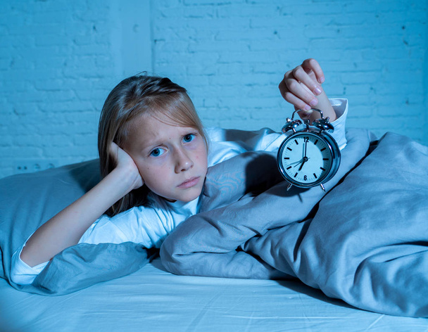 Sweet sleepless little girl lying sad in bed looking at alarm clock having to wake up but feeling tired sleepless in Troubles staying asleep Night Terrors Sleep disorder and Children Insomnia concept. - Foto, Imagem
