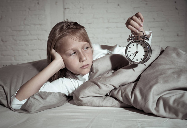 Sweet sleepless little girl lying sad in bed looking at alarm clock having to wake up but feeling tired sleepless in Troubles staying asleep Night Terrors Sleep disorder and Children Insomnia concept. - Foto, Bild