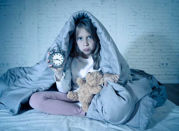 Cute sleepless little girl sitting on bed looking sad and tired having sleeping troubles staying asleep at night or waking too early in the morning in Insomnia Anxiety Sleep Disorders in children. - 写真・画像