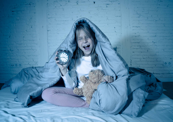 Cute sleepless little girl sitting on bed looking sad and tired having sleeping troubles staying asleep at night or waking too early in the morning in Insomnia Anxiety Sleep Disorders in children. - Foto, afbeelding