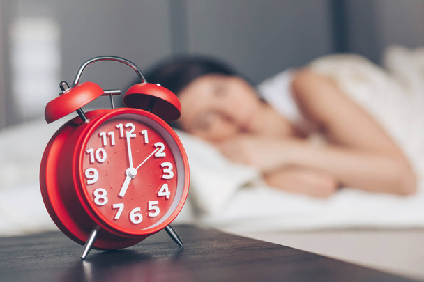 Alarm clock closeup and Young sleeping woman in bedroom at home - Photo, Image