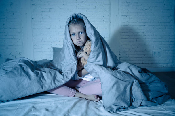 Cute asleep girl screaming and crying after frightening or upsetting dream covering herself with blanket in bed at night in mood dramatic lighting in Sleep terrors Nightmares and Sleeping disorders. - Photo, image