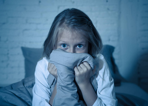 Scared little girl staying sleepless hiding behind the duvet looking horrified in the dark having childhood nightmares in child imagination Sleeping disorders Stress Depression and Insomnia concept. - Foto, afbeelding