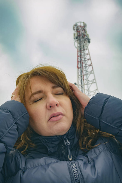 Žena se drží hlavu poblíž Bts. škodlivé záření z koncepce vysílače mobilní sítě - Fotografie, Obrázek