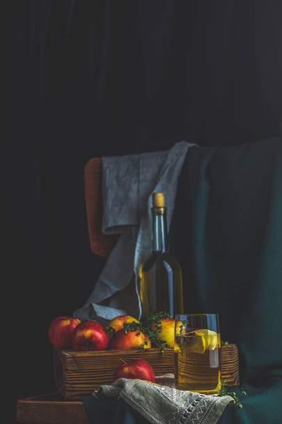 Apfelessig oder Früchtetee mit Apfelscheiben im Glas mit reifen roten Äpfeln im Karton, dunkel rustikaler Vintage-Stil. geringe Schärfentiefe. - Foto, Bild
