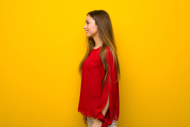 Młoda dziewczyna z czerwoną sukienkę na żółtej ścianie w pozycji bocznej - Zdjęcie, obraz