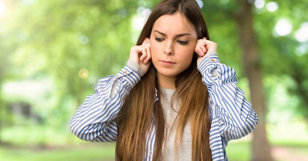 Young girl with striped shirt covering ears with hands. Frustrated expression at outdoors - Foto, Bild