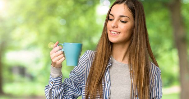 Chica joven con camisa a rayas sosteniendo una taza de café caliente al aire libre
 - Foto, imagen
