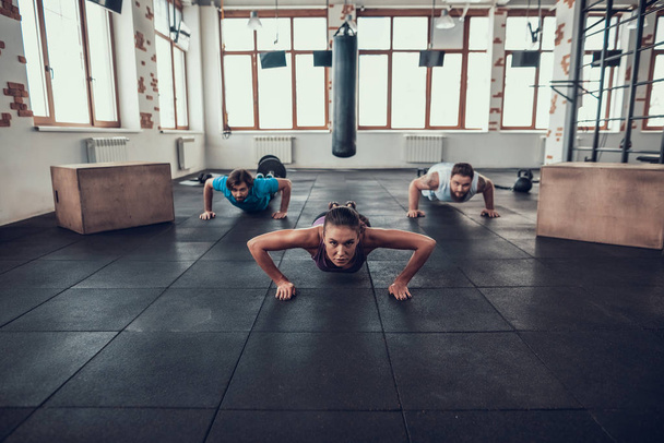 Men And Woman Doing Push Ups. Training Day. Fitness Club. Healthy Lifestyle. Powerful Athlete. Active Holidays. Crossfit Concept. Bright Gym. Comfortable Sportswear. Triceps Muscles. - Photo, image