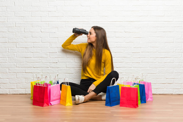 Chica joven con un montón de bolsas de compras y mirando a la distancia con binoculares
 - Foto, imagen