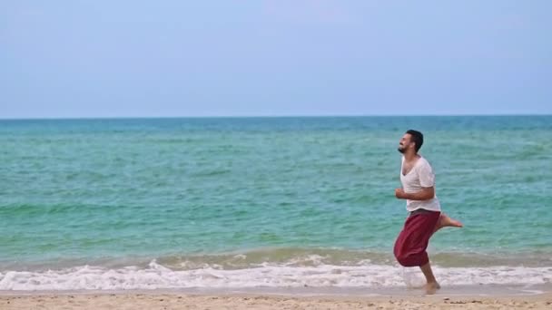 Um jovem e bonito homem corre ao longo da praia numa ilha tropical.
. - Filmagem, Vídeo