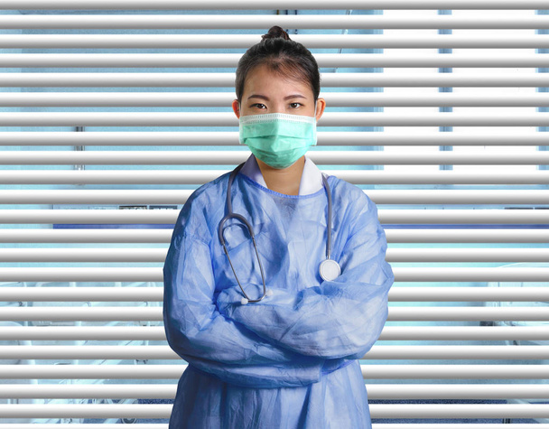 young confident and successful Asian Chinese medicine doctor woman in hospital scrubs and mask posing isolated at venetian blinds patient room in medical health care and corporate physician  - Foto, immagini