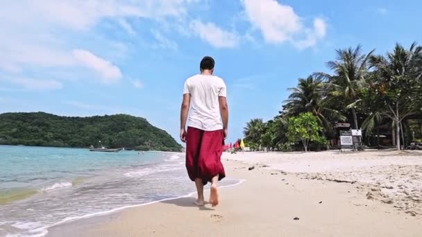 Genç ve yakışıklı bir adam tropik bir adada sahil boyunca yürüyor. - Video, Çekim