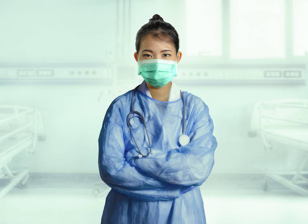 young confident and successful Asian Korean medicine doctor woman in hospital scrubs and mask posing isolated at clinic patient bed in medical health care as corporate physician portrait - Foto, Imagem
