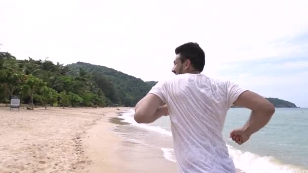 Un uomo giovane e bello corre lungo la spiaggia su un'isola tropicale
. - Filmati, video