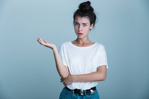 Portrait of a confused young girl presenting copy space isolated over blue background - Foto, Imagen