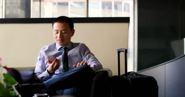 Вид спереди бизнесмена, разговаривающего по мобильному телефону в холле отеля. Азиатский бизнесмен сидит на диване 4k
 - Кадры, видео