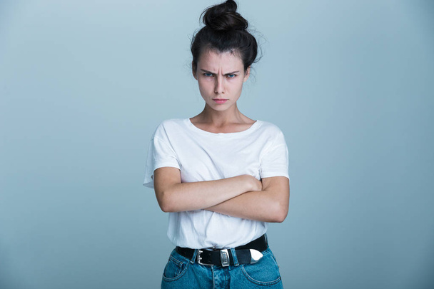 Portrait of an upset young casual girl isolated over blue background, standing with arms folded - 写真・画像