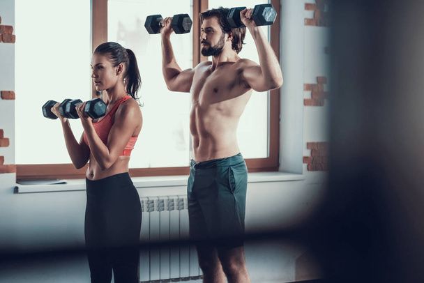 Girl And Guy In Gym Doing Dumbbells Exercises. Training Day. Fitness Club. Healthy Lifestyle. Powerful Athletes. Active Holidays. Crossfit Concept. Sportsman Without T Shirt. Sunny Day. - Foto, afbeelding