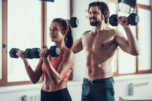 Girl And Guy In Gym Doing Dumbbells Exercises. Training Day. Fitness Club. Healthy Lifestyle. Powerful Athletes. Active Holidays. Crossfit Concept. Sportsman Without T Shirt. Sunny Day. - 写真・画像