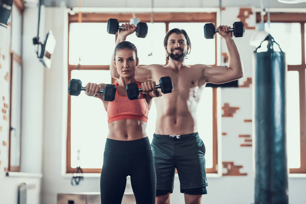 Girl And Guy In Gym Doing Dumbbells Exercises. Training Day. Fitness Club. Healthy Lifestyle. Powerful Athletes. Active Holidays. Crossfit Concept. Sportsman Without T Shirt. Sunny Day. - Zdjęcie, obraz