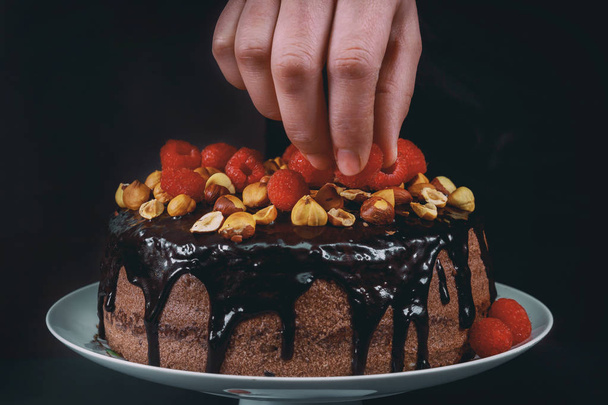 Pastelero en la cocina decorando un pastel de chocolate de frambuesa sobre fondo negro
. - Foto, Imagen