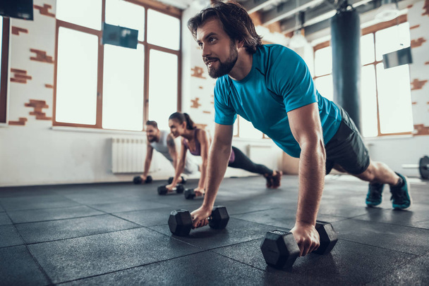 Two Men And Woman Doing Push Ups On Dumbbells. Training Day. Fitness Club. Healthy Lifestyle. Powerful Athlete. Active Holidays. Crossfit Concept. Bright Gym. Comfortable Sportswear. - Фото, изображение
