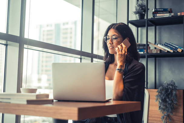 Kaunis liiketoiminnan nainen käyttää kannettavaa tietokonetta ja hymyilee työskennellessään toimistossa
 - Valokuva, kuva