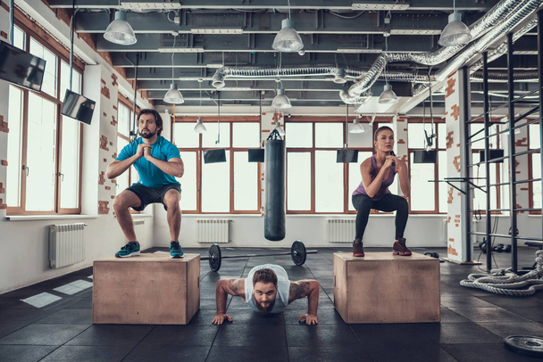Man Doing Push Ups. Guy And Girl Doing Squats. Training Day. Fitness Club. Healthy Lifestyle. Powerful Athlete. Active Holidays. Crossfit Concept. Bright Gym. Comfortable Sportswear. - Foto, immagini