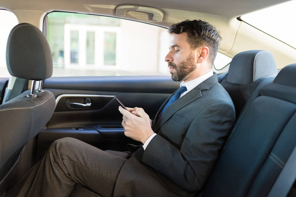 Side view of wealthy CEO using smartphone while traveling in luxury car - Фото, изображение